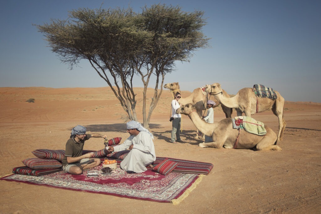 Omanische Männer und Touristen trinken arabischen Kaffee in der Wüste im Oman